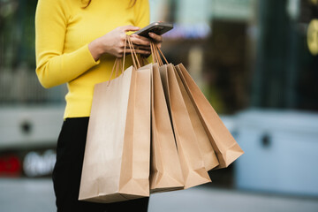 A person wearing a yellow sweater holds several brown paper shopping bags, symbolizing shopping, retail, and eco-friendly lifestyle.