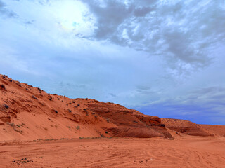 Scenic view of striking red sandstone formations and sand dunes beneath a cloudy blue sky in a...