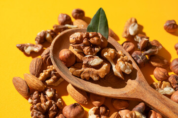 Different nuts, walnut, hazelnut, almond in wooden spoon on yellow background flat lay top view. Mix of tasty healthy nuts, snack, appetizer. Sunlight with long shadows