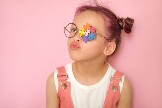 A girl with pink hair and glasses decorated with pieces of colored puzzles. The concept of support and care for people with autism spectrum disorder