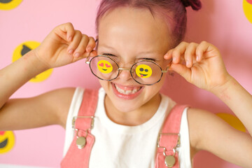 Funny Humorous laughing girl with smiley icons pasted on glasses. World Social Media Day. The problem of children's involvement in cyberspace.