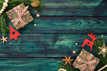 Holiday flat lay with two wrapped gifts, red tree and reindeer cutouts, wooden stars and pine branches on teal rustic background, perfect for Christmas design.