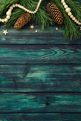 Rustic teal wood background with pine branches, cones, wooden beads and stars. Cozy Christmas flat lay for festive design, greeting card or seasonal decoration.