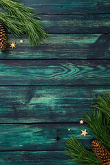 Teal rustic wood background with pine branches, cones and wooden stars in corners. Cozy Christmas flat lay background for festive greeting, seasonal card or winter design.