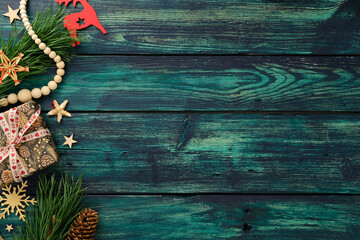 Christmas holiday composition with gift, pine branches, wooden stars, reindeer and straw ornament on teal wood background, ideal for seasonal card or banner.