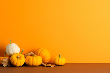 Pumpkins and dry leaves on orange background. Minimalist autumn still life symbolizing harvest, Halloween, and Thanksgiving seasonal decor.