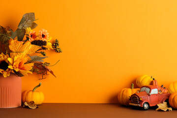Festive fall bouquet with pumpkins, leaves, and toy truck on orange background. Seasonal harvest still life for Thanksgiving and autumn home decor.