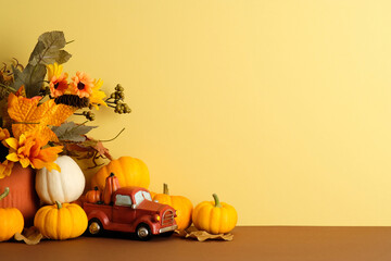 Pumpkins, autumn bouquet, and red toy truck on yellow and brown background. Seasonal harvest still life for Thanksgiving and fall home decor.