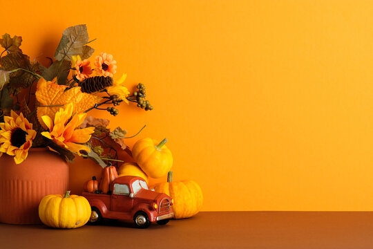 Autumn vase with sunflowers, pumpkins, and red truck decor on orange background. Warm harvest still life perfect for Thanksgiving and fall celebration theme