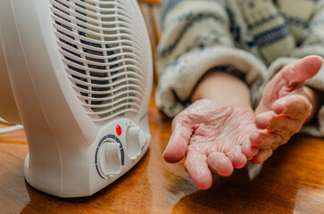 Elderly Hands Warming by Electric Heater Indoors