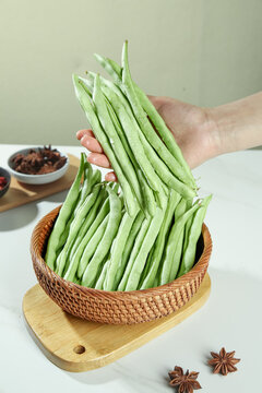 Fresh Green Beans in Wicker Basket with Hand Holding Vegetables on Wooden Board