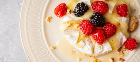 Melted camembert cheese topped with raspberries, blackberries, walnuts and honey. Healthy dessert. Shallow depth of field.