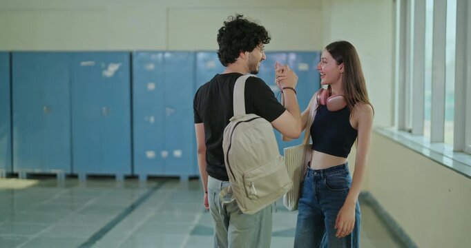 Indian young adult gen z pupil girl walk meet boy guy give high five talk spend break time campus place. Happy male man female lady casual gossip share do greet hello enjoy new day college hallway  