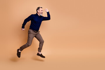 Mature businessman wearing formal attire poses energetically against a beige background exuding style, confidence and charm