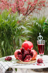 Fresh Pomegranate with Red Seeds and Juice Glass on Garden Table