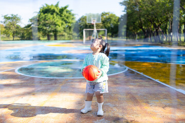 A cute little Asian girl is having fun playing basketball on the basketball court.