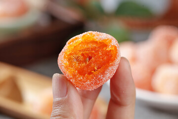 Sugar coated dried kumquat candy held in hand - traditional Asian sweet confection with rock sugar coating
