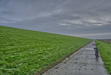 Bicycle resting on deich path with green grass and sheep, east frisia, germany, under a grey cloudy sky