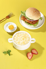 Fresh corn kernels porridge with burger and strawberries on yellow background - healthy meal concept
