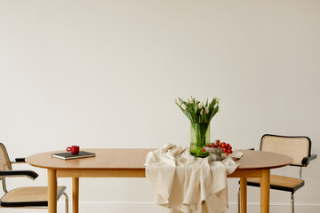 Modern dining room with wooden table, cane chairs and green tulips in a glass vase. Soft light and balanced, minimalist design.
