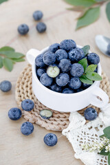 Fresh Blueberries in White Cup with Green Leaves on Rustic Wood Background