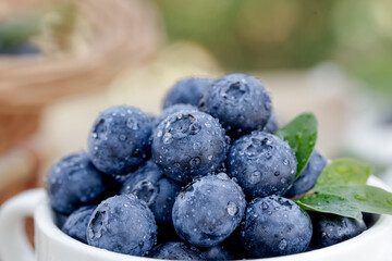 Fresh Wet Blueberries in Bowl with Green Leaves on Wooden Table