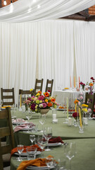 colorful wedding table setting. Multicolored flower arrangements, vases, napkins, green tablecloth, fabric suspended ceilings