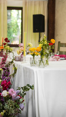 colorful wedding table setting. Multicolored flower arrangements, vases, napkins, green tablecloth, fabric suspended ceilings