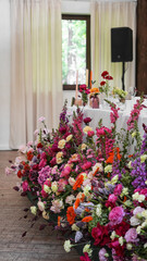 Colorful wedding flower arrangement in front of the bride and groom's table. Ranunculus, gerbera, snapdragons, roses, carnations, peonies
