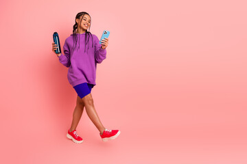 Smiling young woman holding phone and bottle, dressed in sporty casual wear, standing in front of...
