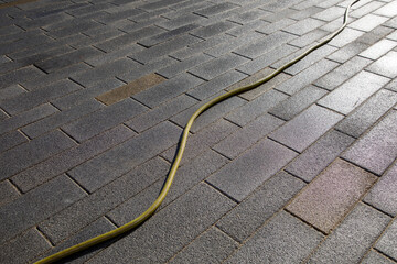 Wet paving stone surface with yellow hose, maintenance element of outdoor area. Use in municipal...