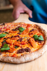 Homemade pizza being served on a wooden peel, person holding fresh baked italian food, traditional crust