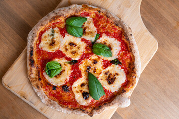 Freshly baked neapolitan pizza margherita on a wooden board ready for serving, showcasing italian cuisine and delicious food. Overhead plane