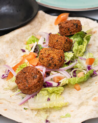 Falafel balls on a whole wheat wrap with fresh salad, sliced tomatoes, red onions, and crisp lettuce