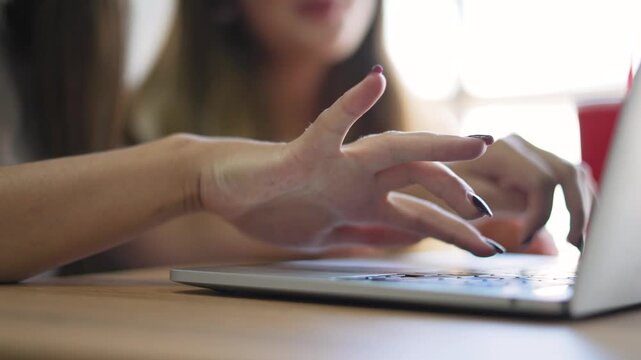 Typing on laptop keyboard with manicure hand by woman at wooden desk in office work environment showing computer use for business task and remote work communication closeup of hand typing on keyboard