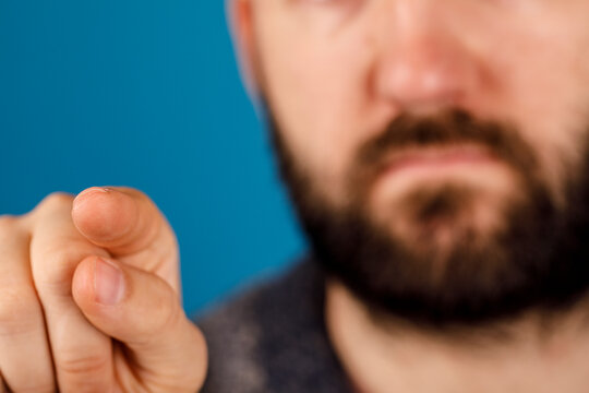 Close-up shot of a man's hand pointing directly at the viewer, with a blurred face and blue background. Ideal for concepts like choice, directio