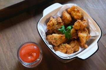 A bowl of crispy fried chicken bites served in a white ceramic dish lined with parchment paper, garnished with fresh parsley.