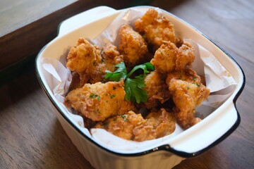 A bowl of crispy fried chicken bites served in a white ceramic dish lined with parchment paper, garnished with fresh parsley.	