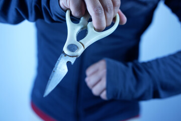 Dangerous Man Holding Sharp Scissors in the Dark, Murder Concept. Scissors in a man's hand attack from the darkness, close-up. The criminal with a sharp weapon threatens to stab.