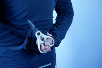 A person's hand is holding scissors behind his body, the concept of being defensive or threatening. Photo illustration of murder, robbery