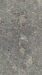 Detailed full-frame background texture of rough, damaged, dark gray asphalt pavement featuring embedded small gravel and vertical lines of erosion and cracking. Construction concept