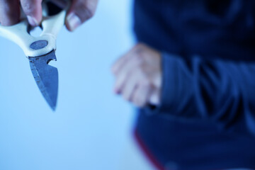 An aggressive hooded youth brandishes scissors, preparing to stab, his face invisible against the black background. A killer with a knife in his hand in the darkness. Attacking the victim.