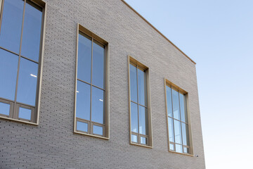 Gray brick facade with vertical windows and beige frames under clear sky. Architectural exterior for commercial building visuals, websites, web design, presentations, reports. Real photo