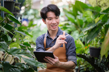 Young man in apron using digital tablet and stylus while working in a lush greenhouse, blending modern technology with sustainable gardening practices.