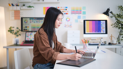 Focused graphic designer using laptop and pen tablet in modern workspace.