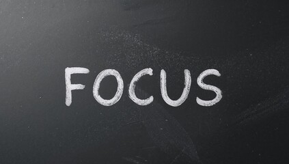 Chalkboard message White word Focus contrasted against a dark textured surface.