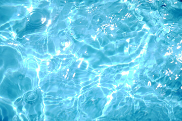 A serene, top-down view of shimmering blue water with sunlit ripples, creating a beautiful abstract pattern. The clear surface evokes feelings of calmness, purity, and refreshment.

