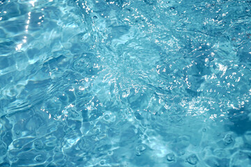 A serene, top-down view of shimmering blue water with sunlit ripples, creating a beautiful abstract pattern. The clear surface evokes feelings of calmness, purity, and refreshment.

