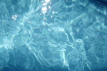 A serene, top-down view of shimmering blue water with sunlit ripples, creating a beautiful abstract pattern. The clear surface evokes feelings of calmness, purity, and refreshment.

