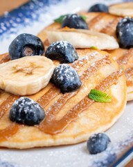 Pancakes with blueberries, banana slices, caramel sauce, and powdered sugar for breakfast dish